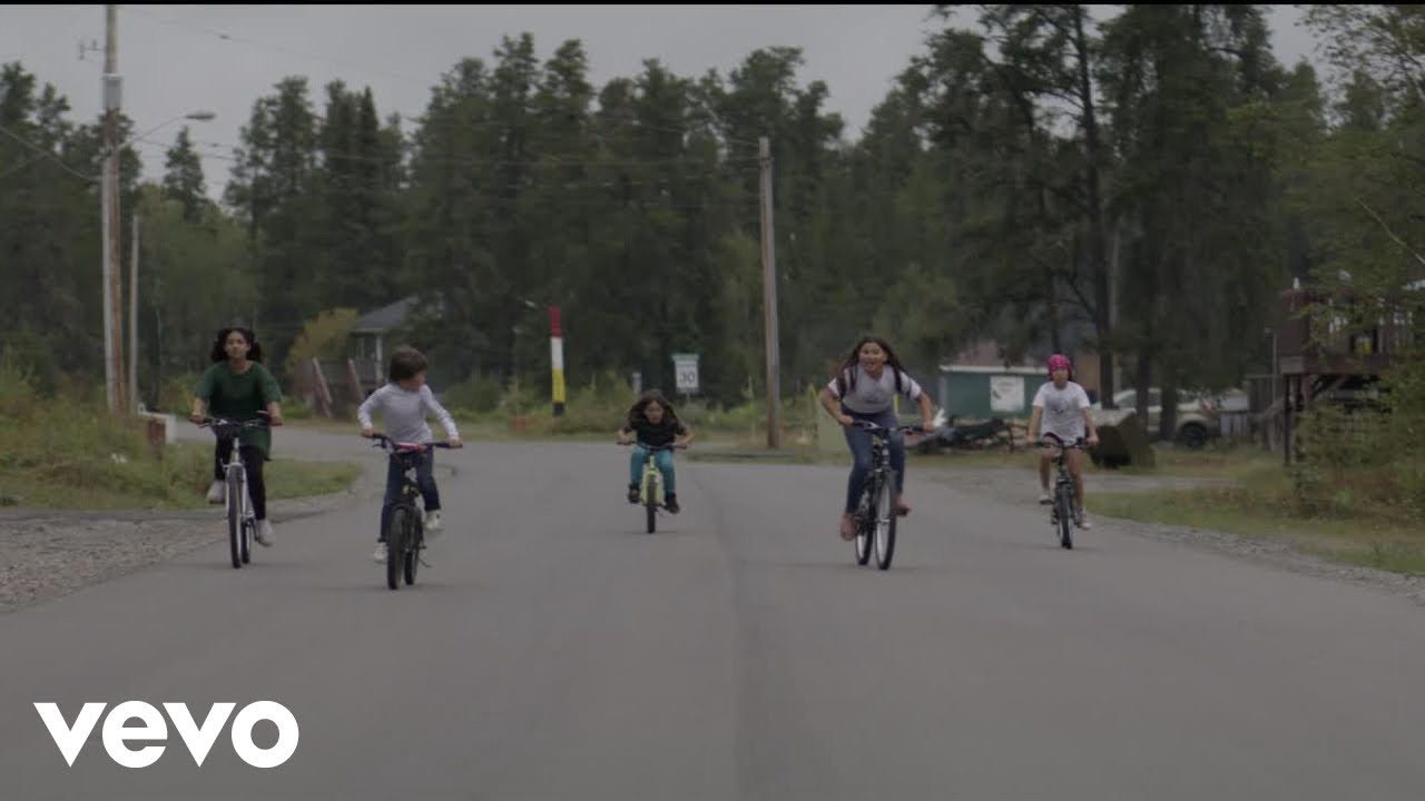 Youth riding bikes down a road in the Friends music video